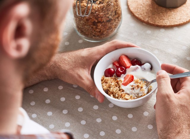 Man scooping in yogurt fruit granola breakfast bowl