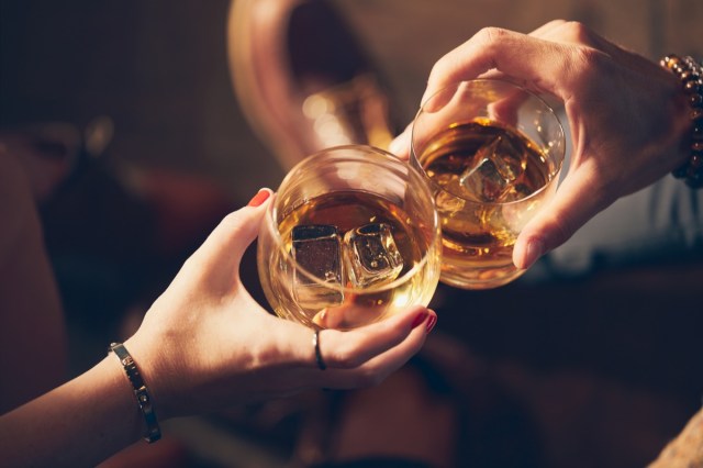 a couple makes a toast with two glasses of whiskey