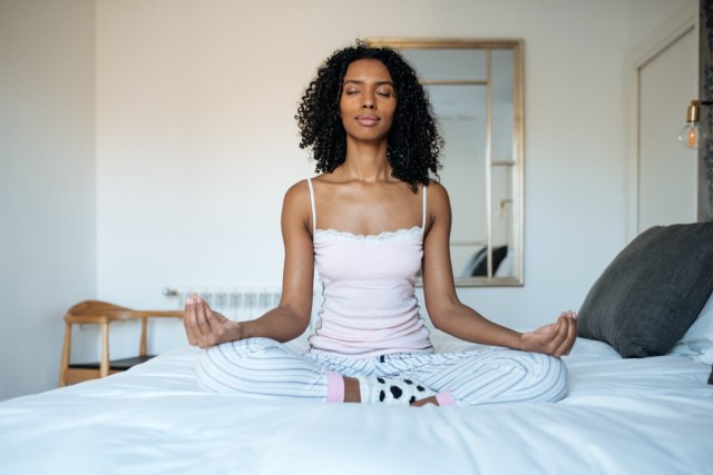 woman sitting in lotus position on bed meditating
