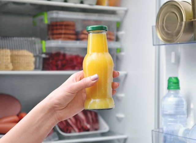 unhealthy orange juice bottle held in front of fridge