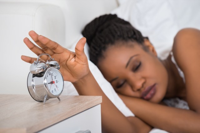 woman turning off alarm while sleeping on bed