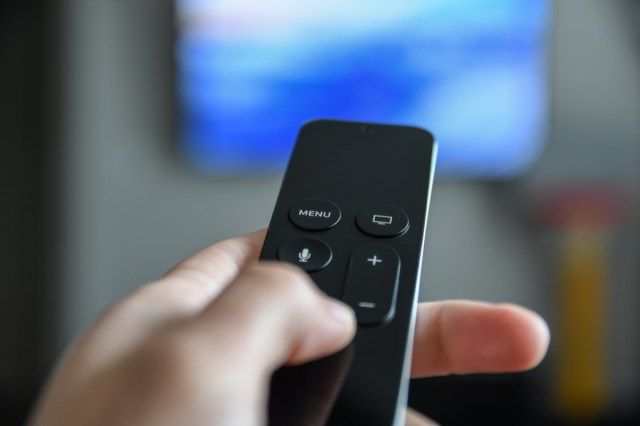 man using remote control to switch channels. close up hand holding big screen tv remote.