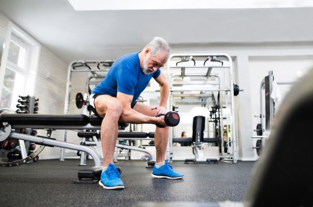 senior man in sports clothing in gym working out with weights