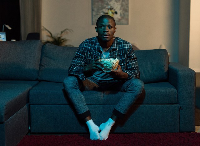 man watching tv on couch holding popcorn bowl