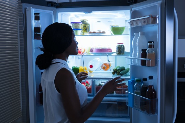 woman taking out bottle from open refrigerator