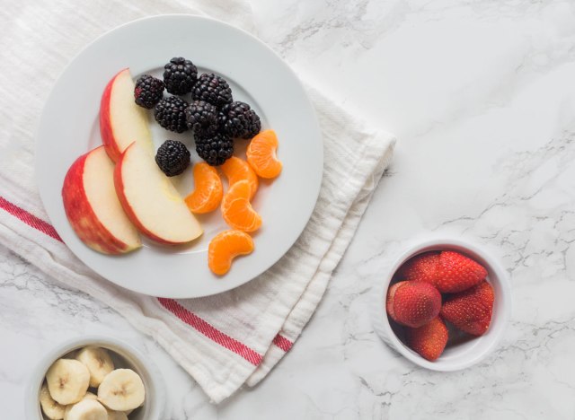 plate of fruit - apple slices tangerines blackberries - and bowls of strawberries bananas