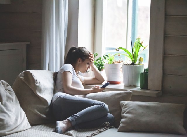 woman sitting on bed looking at phone bored and in a bad mood