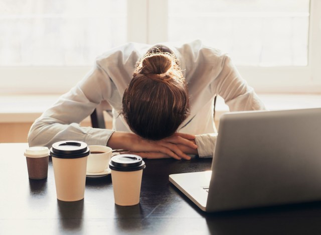 tired woman working at her desk drinking too much coffee