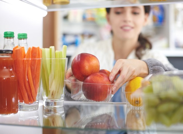 woman rearranging her refrigerator to put healthy fruits vegetables healthy snack in front