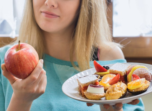 woman choosing healthy apple instead of junk dessert as a food exchange to cut calories