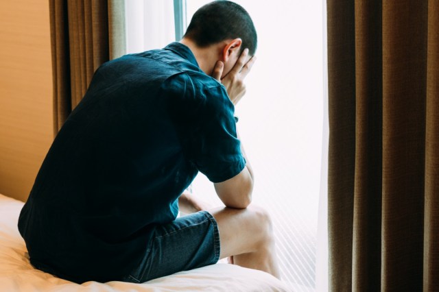 depressed man with problems sitting alone head in hands on the bed and crying