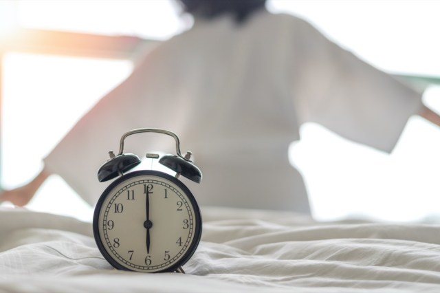 woman on bed wake up stretching in bedroom with alarm clock at 6.00 a.m. morning.