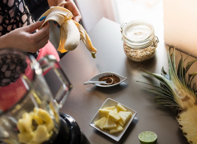 woman peeling a banana to make a pineapple smoothie