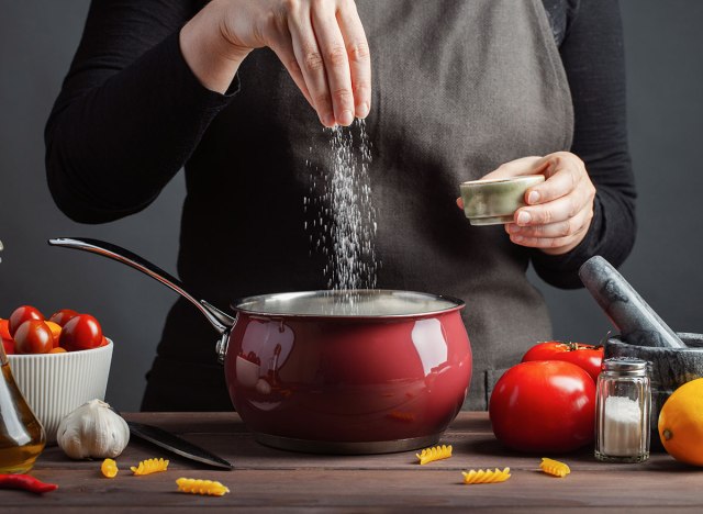 hands add salt to pasta water