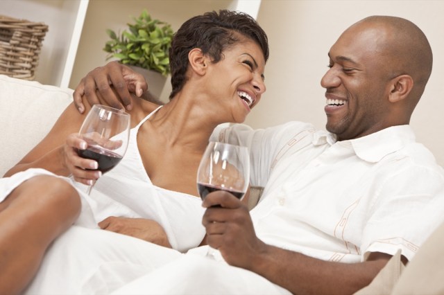 couple sitting at home together laughing and drinking glass of red wine