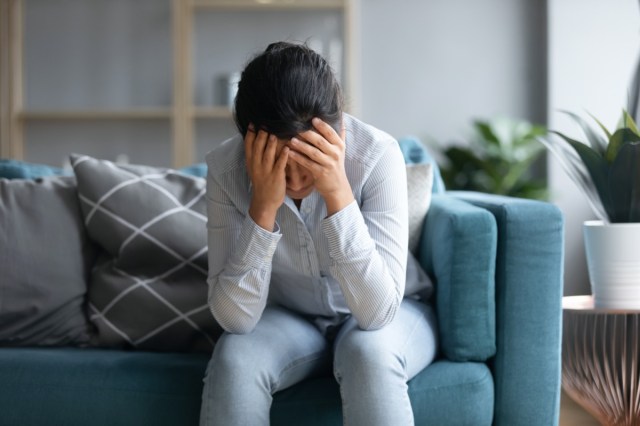 depressed indian woman holding head in hands and sitting alone on sofa at home