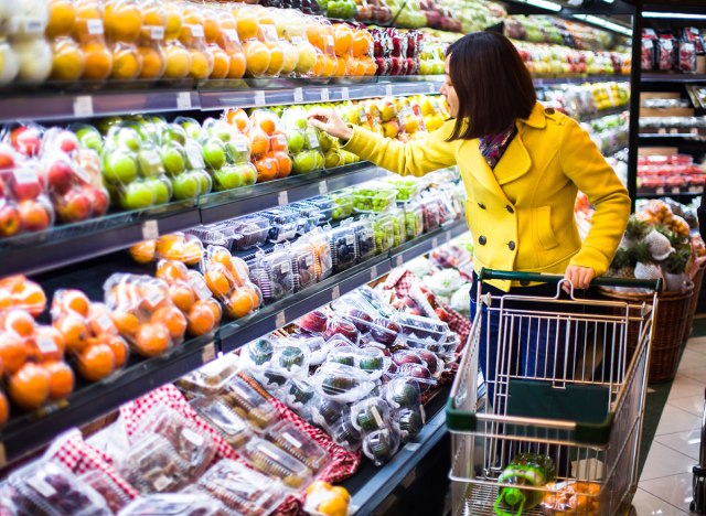 woman wearing a yellow coat scans producing part of a grocery store