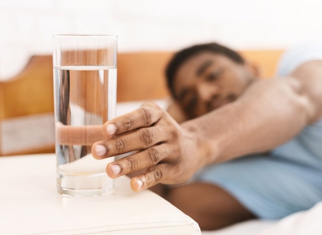 black man reaching for a glass of water from his bed in the morning