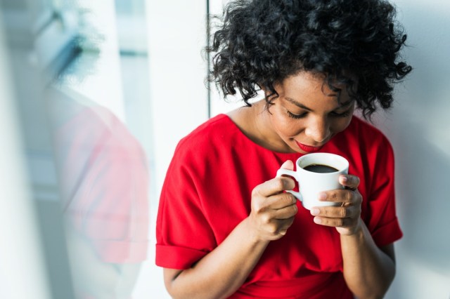 a close-up of a woman standing by the window holding a cup of coffee.