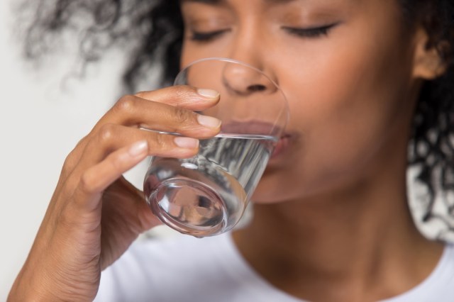 close up focus on female hand holding glass african woman drinking still water