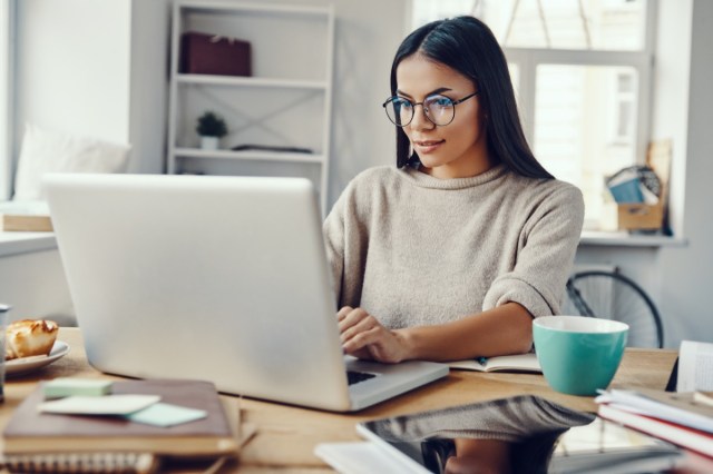 woman in casual clothing using laptop and smiling while working indoors