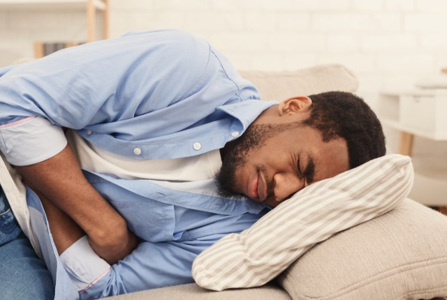 african-american man suffering from stomach ache, lying on sofa at home