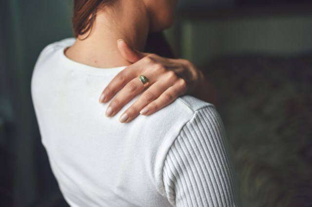 woman is touching her stiff shoulder.
