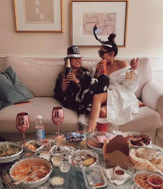 shay mitchell and her friend holding champagne and surrounded by food