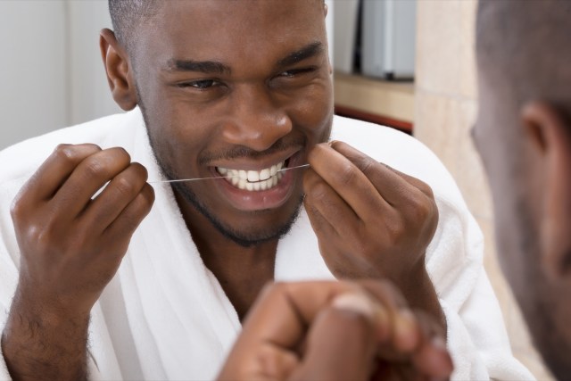 young man cleaning his teeth in front of mirror