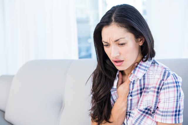 pretty brunette coughing on couch at home in the living-room.