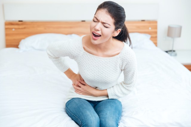 woman sitting on the bed and touching her left side in pain at home