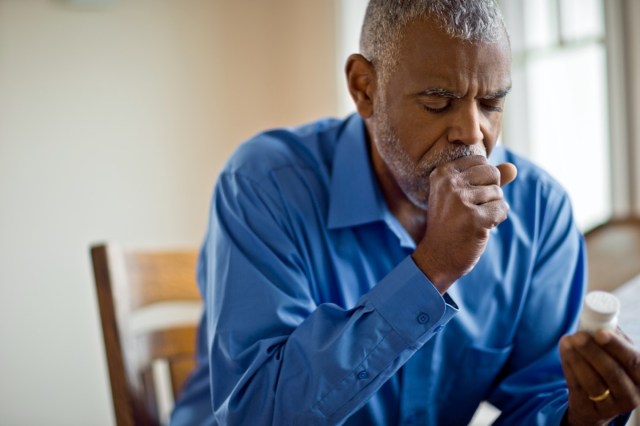 sick man looks at pill bottle whilst coughing.