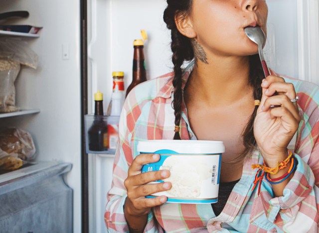 woman eating ice cream straight out of the pint and in front of the freezer