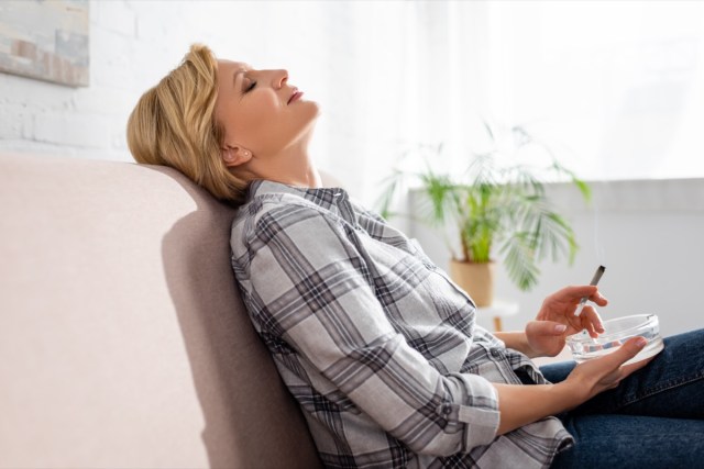 a mature woman with closed eyes sitting on the couch and holding the line with legal marijuana.