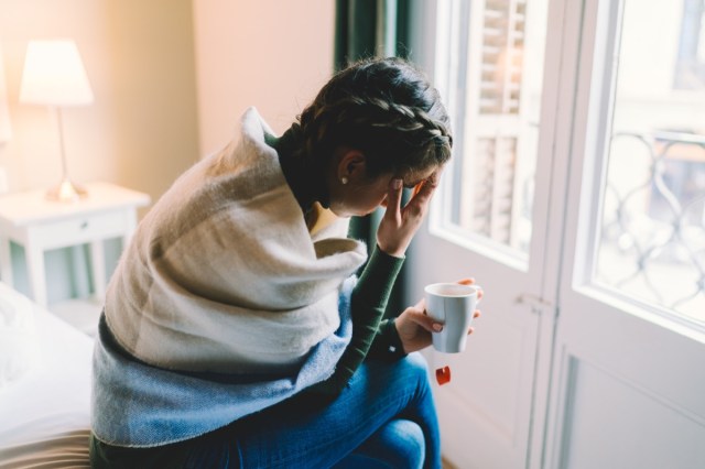 woman with temperature staying home wrapped in scarf and drinking hot tea.