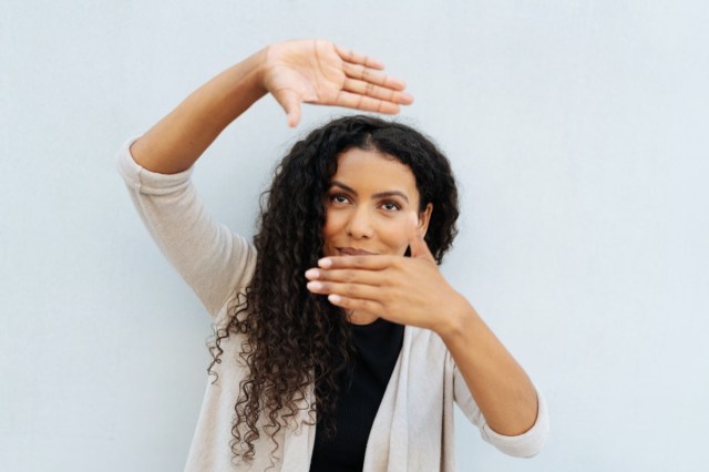 young woman making a frame gesture with her hands as she visualises a new project standing against a white wall