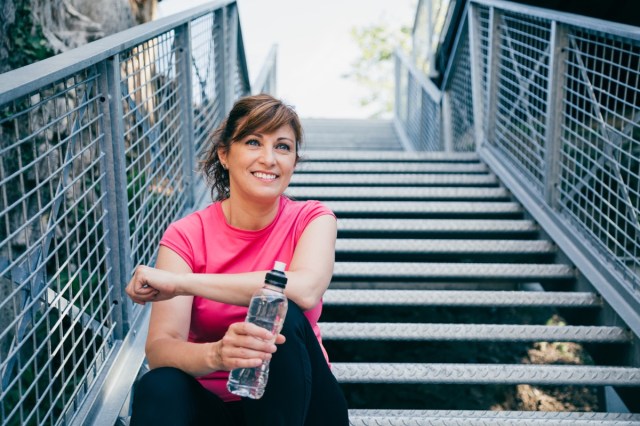 middle-aged woman sitting on metallic stairs relaxing before driving outdoors with a water bottle