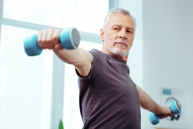 strong fit aged man looking at his hand while exercising with dumbbells