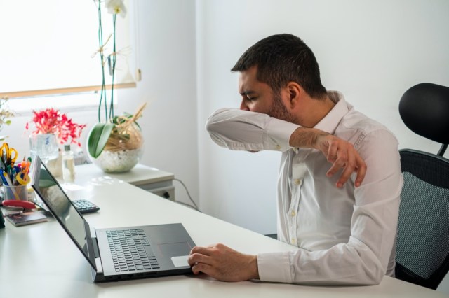 young business man sneezing. coughing into his sleeve or elbow to prevent spread covid-19. corona virus