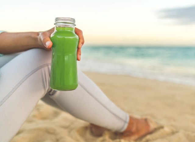 woman holding green juice on the beach