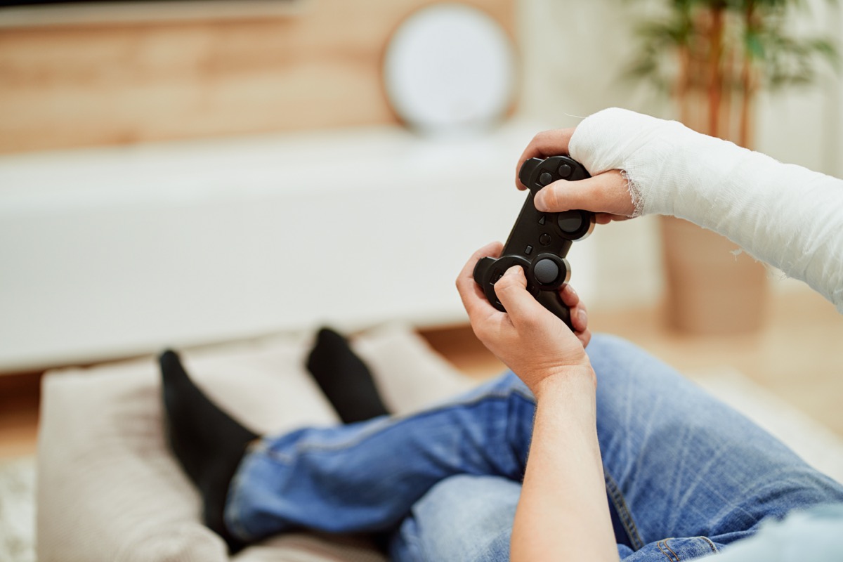 man with broken arm in plaster cast holding control and playing in video games in front of tv.