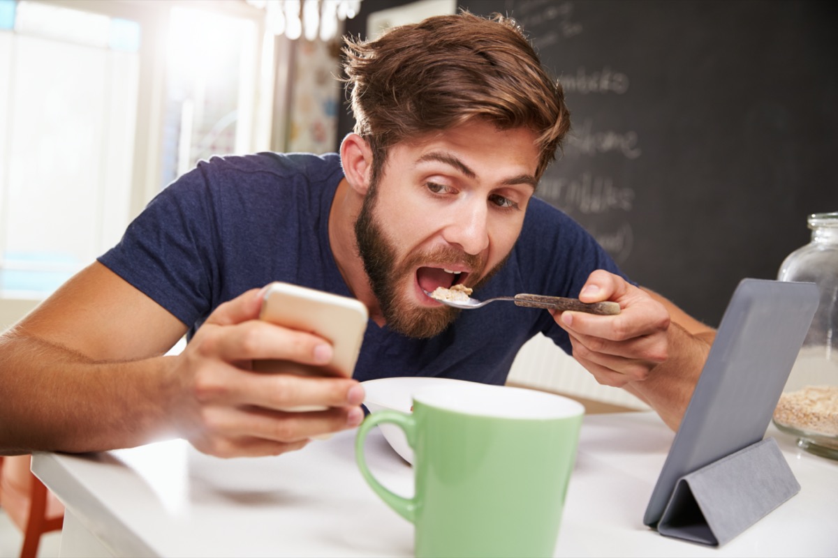 man eating breakfast whilst using digital tablet and phone