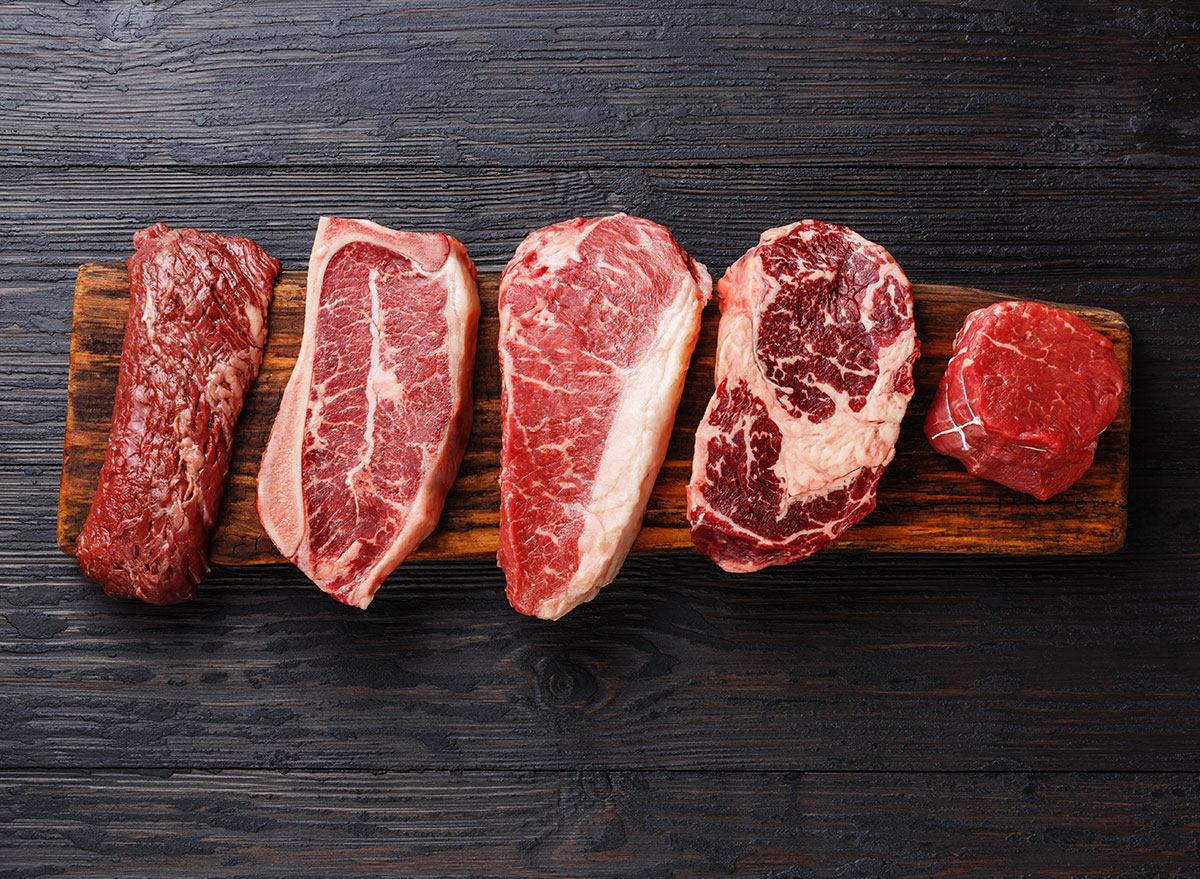 plates of different cuts of red meat on wooden cutting board