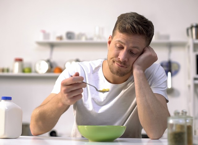 bored man eating bowl of cereal in the kitchen