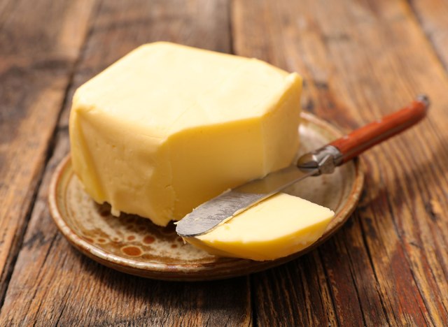 block of butter with slice out of it from knife on platter