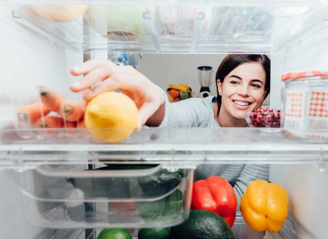 woman reaching into fridge to grab healthy food lemon