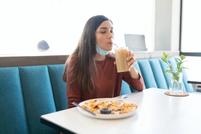 hispanic young woman having drink in cafe during coronavirus outbreak