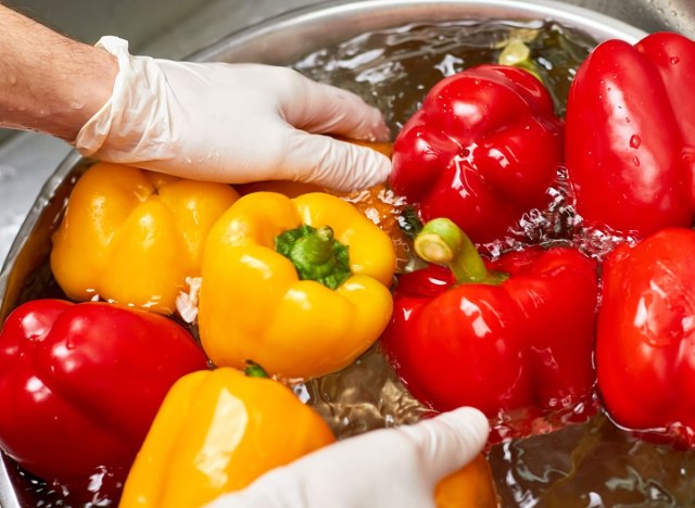 man wearing gloves washing peppers vegetables produce in large bowl water