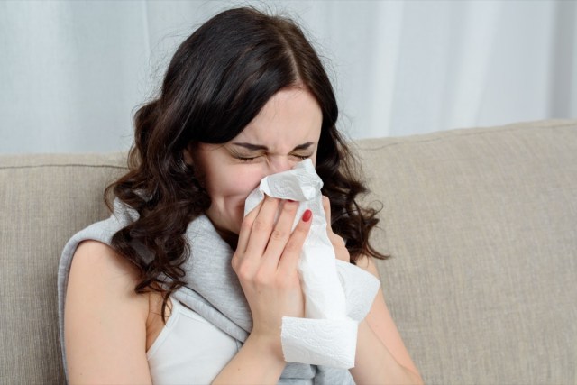 portrait of ill woman caught cold, feeling sick and sneezing in paper wipe