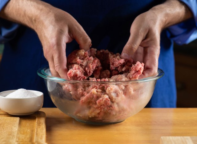 season ground beef mixing with hands in glass bowl